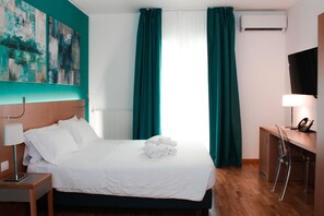 A hotel room with a bed, a desk, a chair, a telephone, and an air conditioning unit.