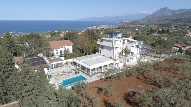A modern multi-story building with a swimming pool, surrounded by trees and a view of the sea. - Principe Alogna Wellness & Spa (Altavilla Milicia)