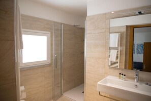 A modern bathroom with a glass-enclosed shower, a large mirror, and a sink with toiletries.