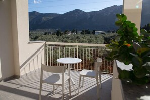 A balcony with a white table and two chairs, overlooking a mountainous landscape.