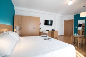 A hotel room with a large bed, wooden wardrobe, desk, and a TV mounted on the wall.