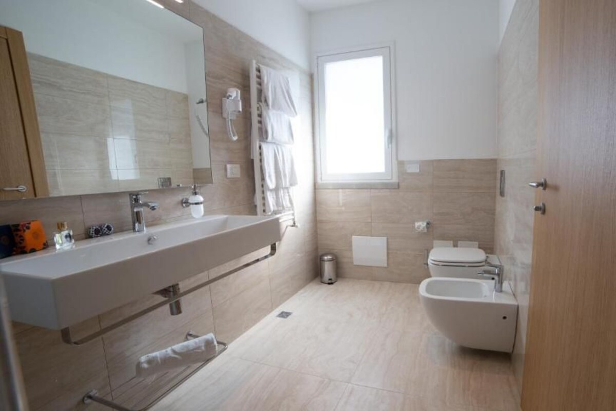 A modern bathroom with a large mirror, a sink, a toilet, and a bidet.