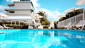 A swimming pool with white lounge chairs and umbrellas, surrounded by a white fence and greenery. - Principe Alogna Wellness & Spa (Altavilla Milicia)