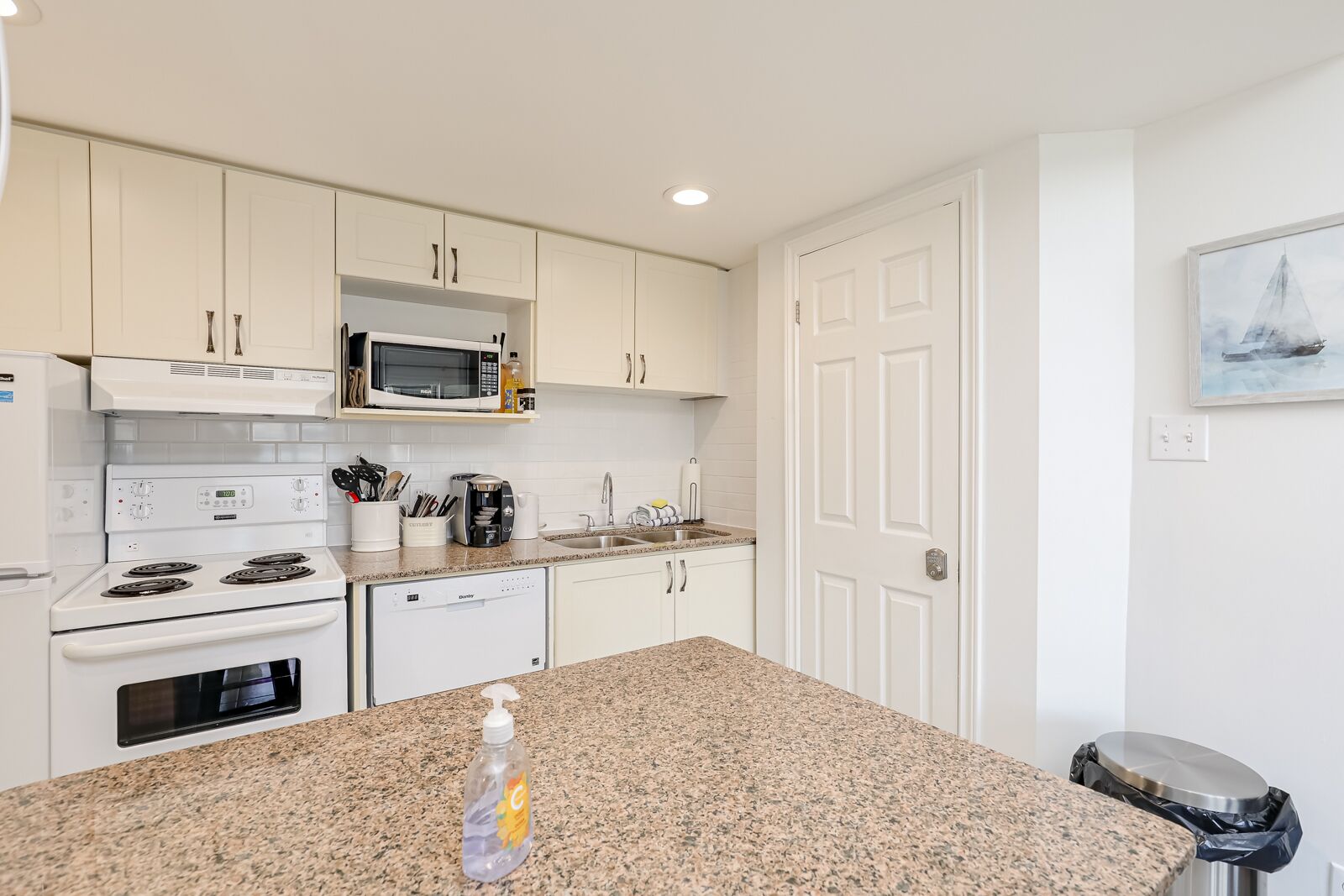 A modern kitchen with white cabinets, a granite countertop, a microwave, a stove, and a dishwasher.