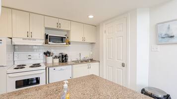 A modern kitchen with white cabinets, a granite countertop, a microwave, a stove, and a dishwasher.