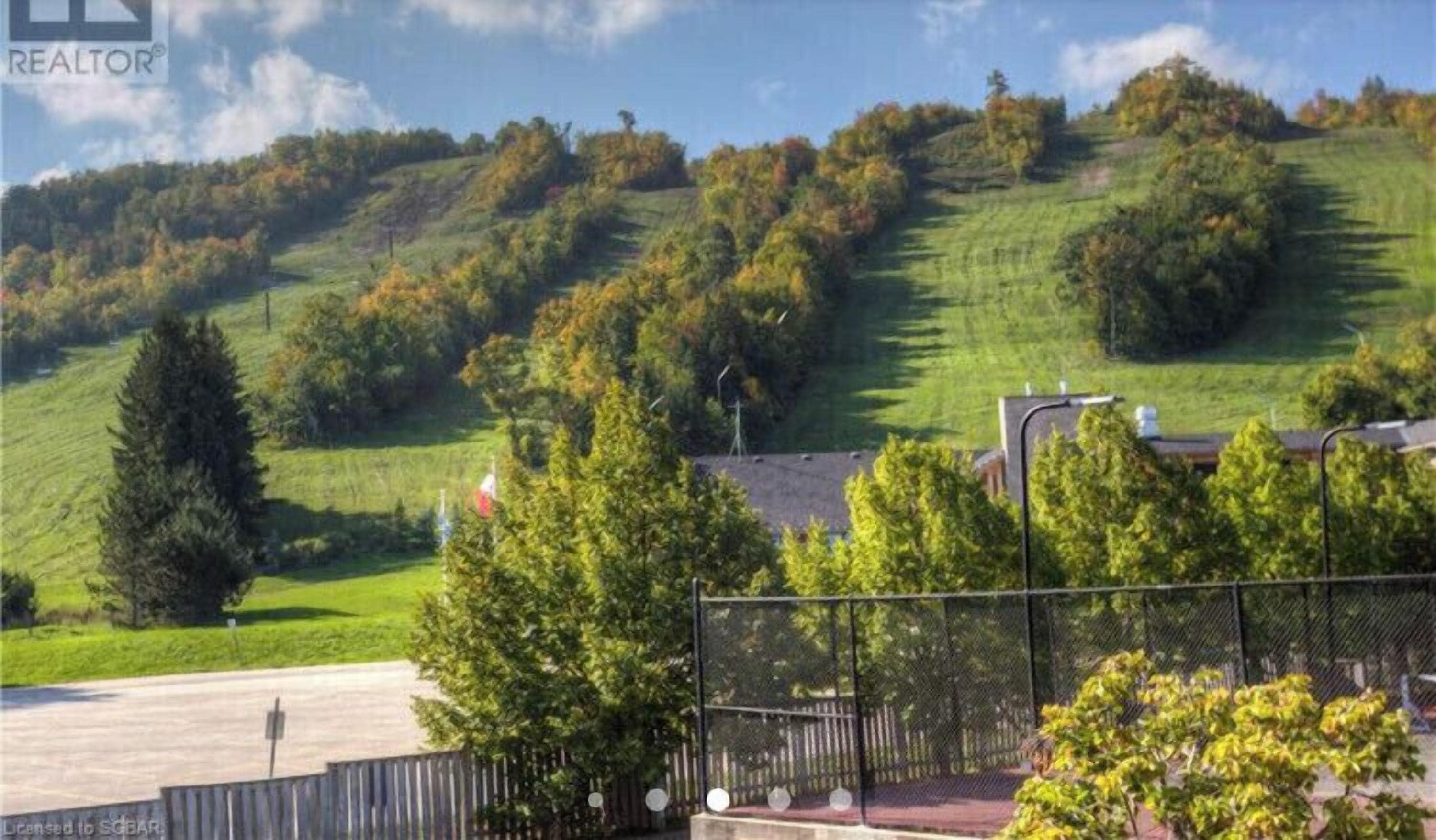 A residential area with a grassy hill, trees, and a fence.