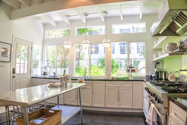 A kitchen with white cabinets, a large island, stainless steel appliances, and large windows with views of greenery. - CASABLANCA- Grand Edwardian View Home (San Francisco)