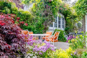 A patio with a table and chairs, surrounded by lush greenery and flowering plants. - CASABLANCA- Grand Edwardian View Home (San Francisco)