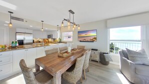Une cuisine moderne avec des meubles blancs, un réfrigérateur en acier inoxydable et un coin repas comprenant une table en bois et des chaises en osier.