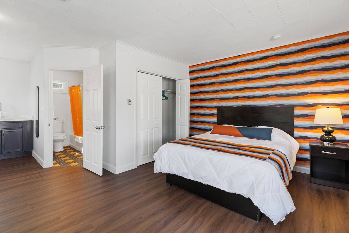 A bedroom with a bed, a nightstand, a bathroom with a toilet and shower, and a hallway.