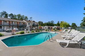 A swimming pool with lounge chairs, a fenced area, and a row of buildings in the background. - Wagon Wheel Motel (Saco)