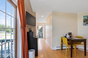 A room with a dining table, chairs, a TV mounted on the wall, and a window with curtains. - Wagon Wheel Motel (Saco)