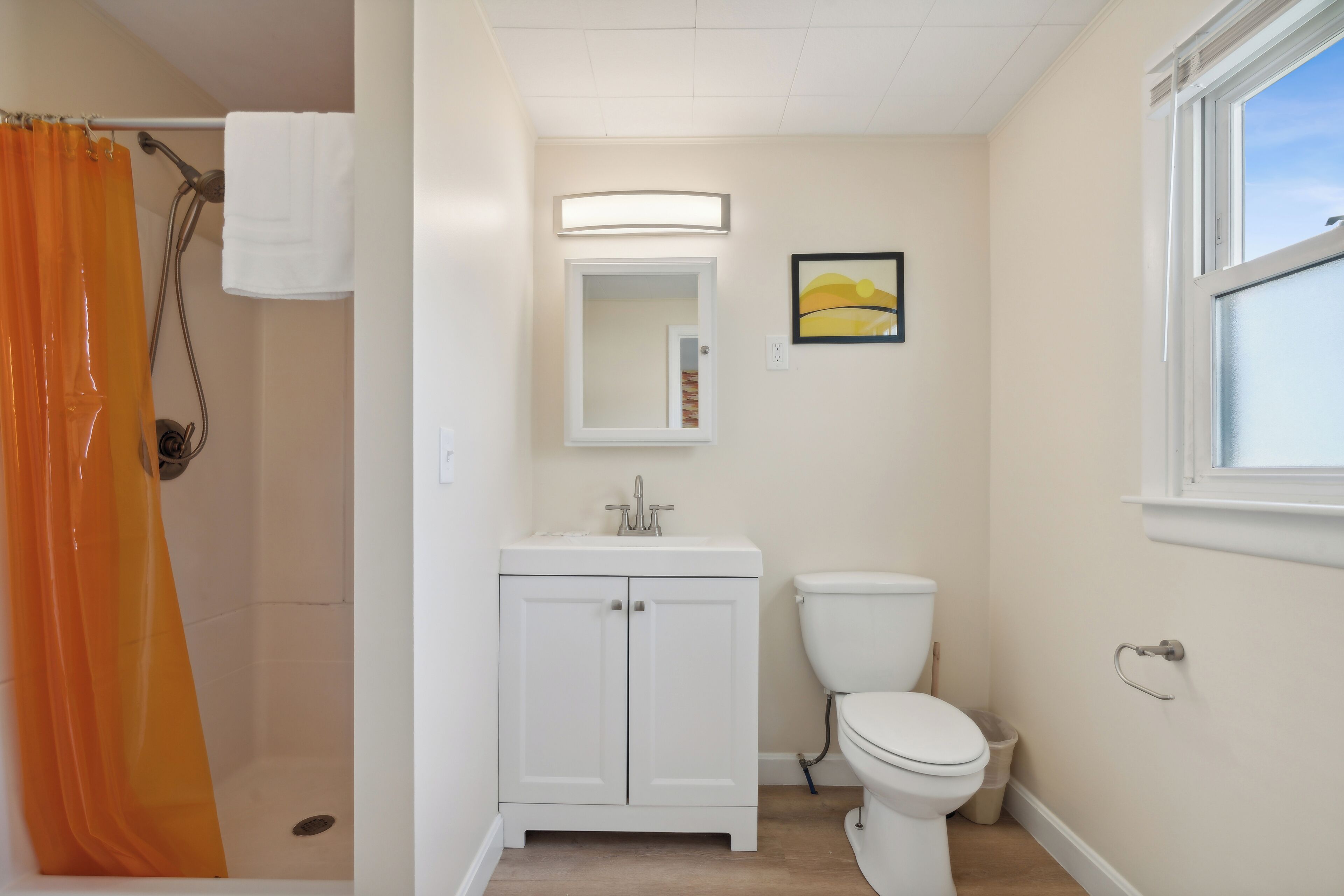 A bathroom with a shower, toilet, sink, and a window.