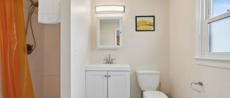 A bathroom with a shower, toilet, sink, and a window.