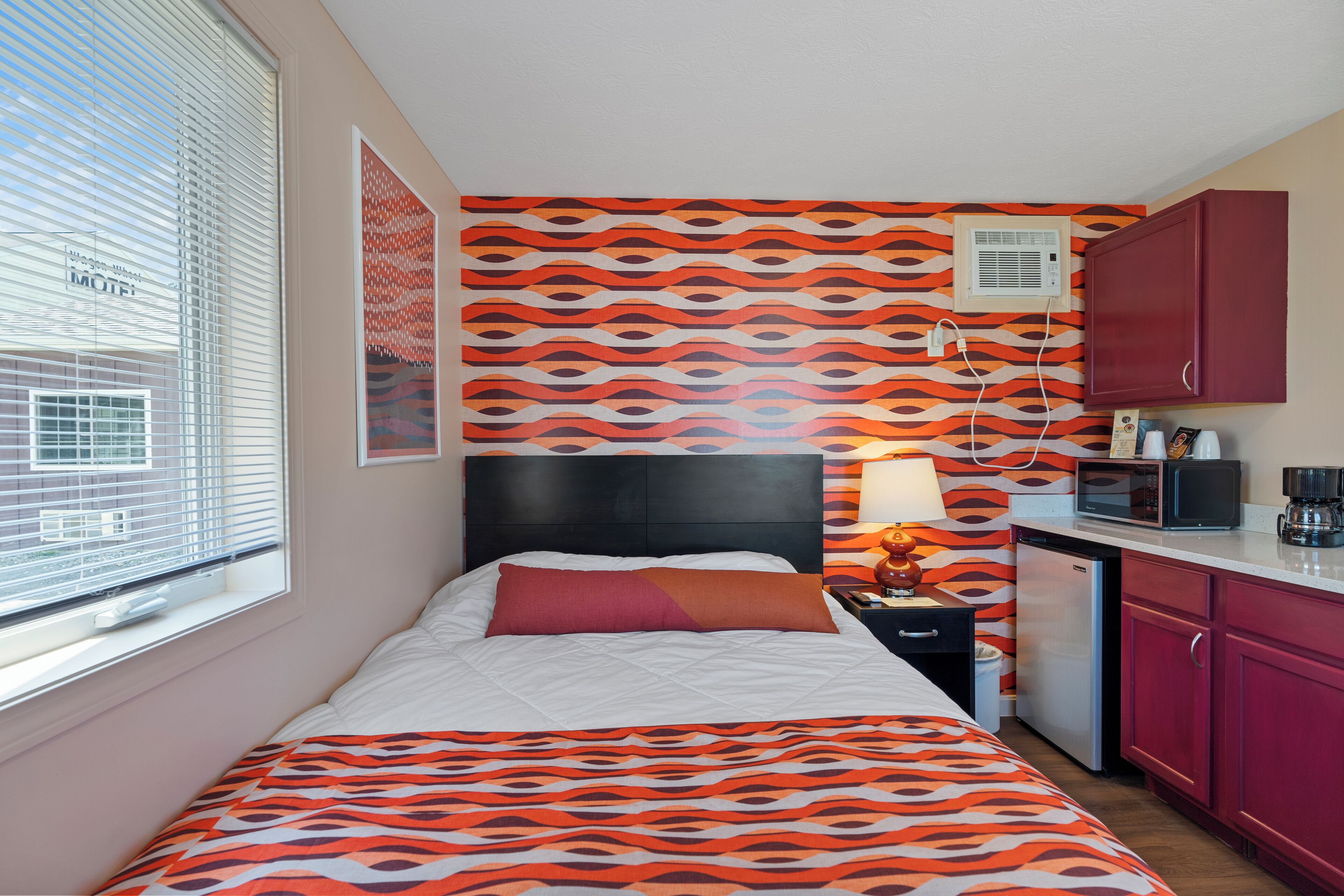 A bedroom with a bed, a nightstand, a lamp, a microwave, and a coffee maker.