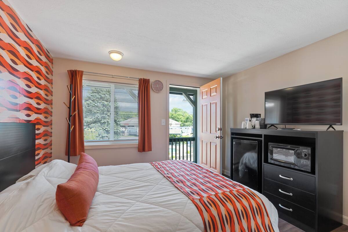 A bedroom with a bed, a TV, a microwave, and a balcony view.