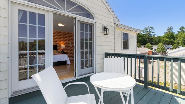 A covered outdoor area with a table and chairs, a sliding glass door leading to a bedroom, and a view of the surrounding neighborhood. - Wagon Wheel Motel (Saco)