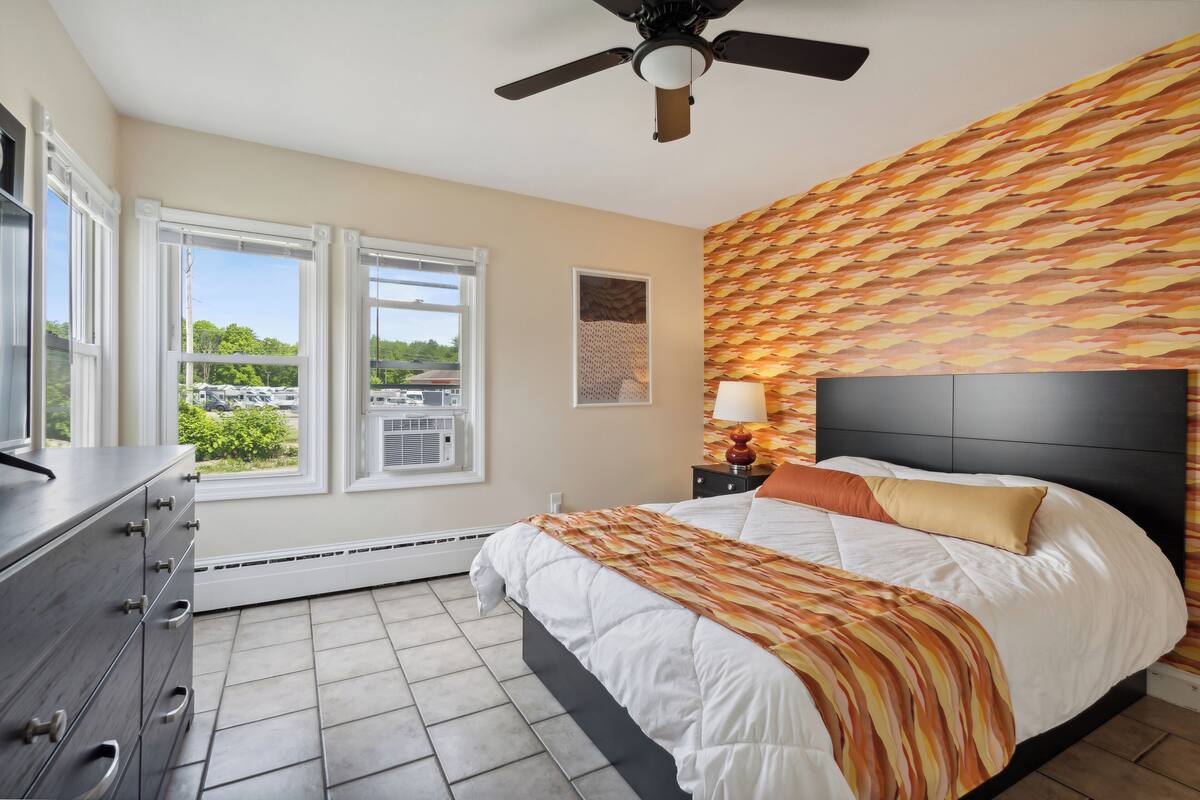 A bedroom with a bed, a dresser, a ceiling fan, and a window with a view of the outside.