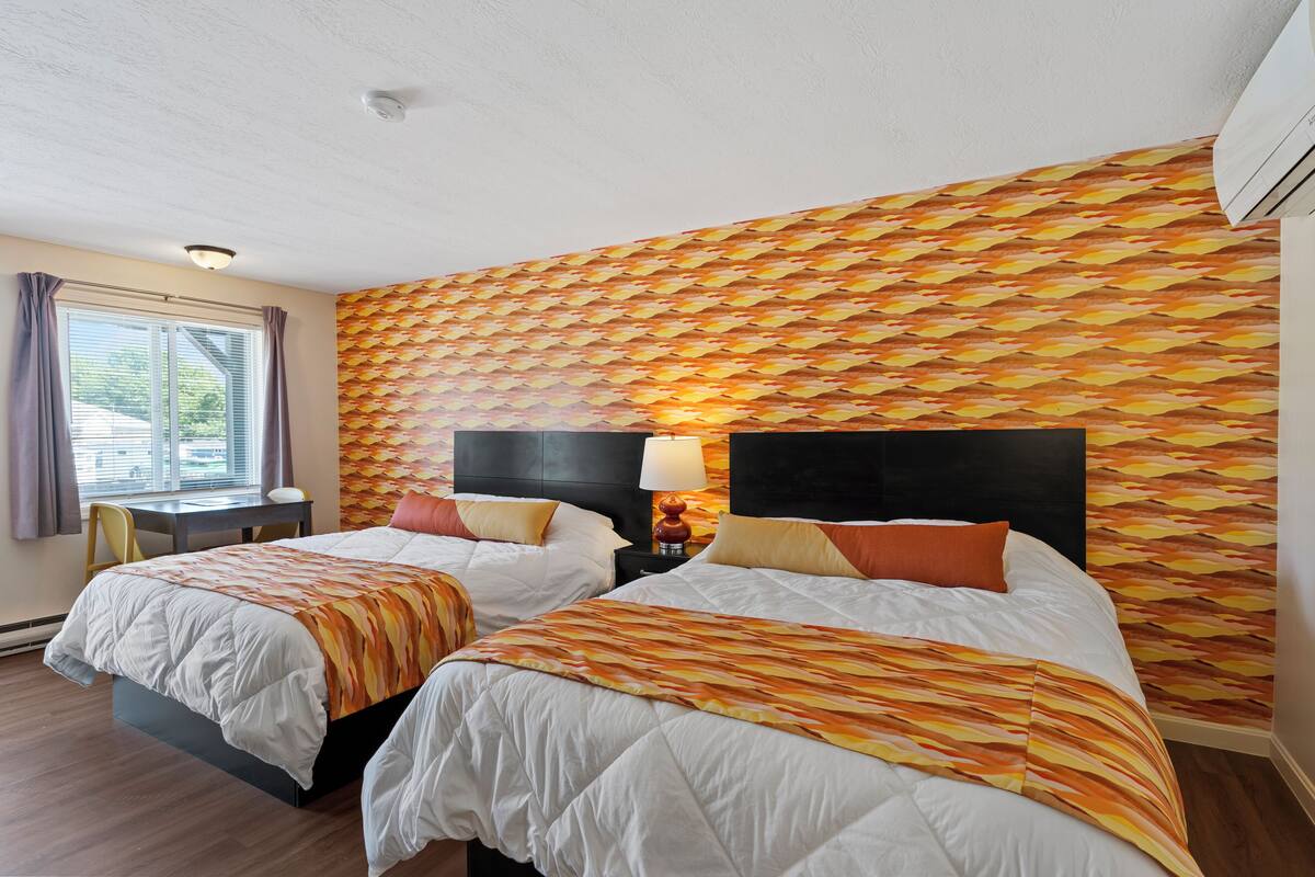 A hotel room with two beds, a desk, and a window.