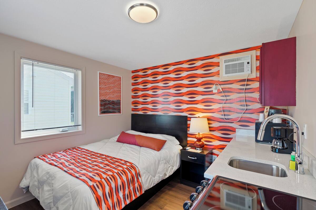 A bedroom with a bed, bedside table, lamp, and a view of the city through a window.