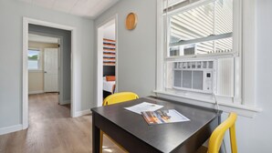 A room with a dining table, two yellow chairs, a clock on the wall, and a window with blinds. - Wagon Wheel Motel (Saco)