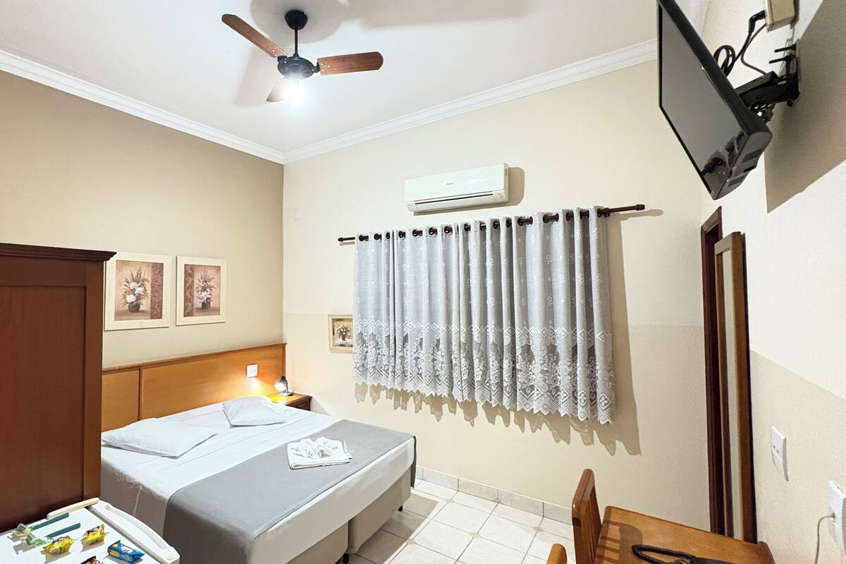 Une chambre d’hôtel équipée d’un lit, d’un bureau, d’une chaise, d’un ventilateur de plafond, d’un climatiseur et d’un téléviseur fixé au mur.