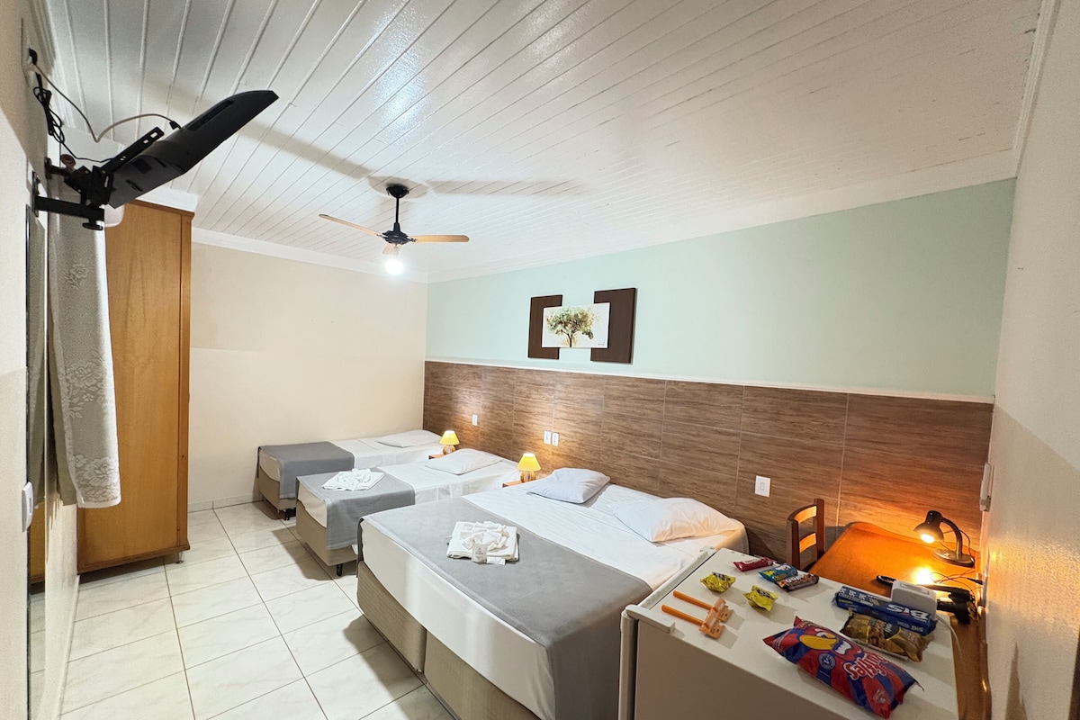A hotel room with two beds, a ceiling fan, a small table with snacks, and a wooden headboard.