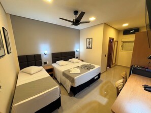 A hotel room with two beds, a desk, a chair, a ceiling fan, and a door leading to another room. - Hotel Casa Grande (Orlandia)