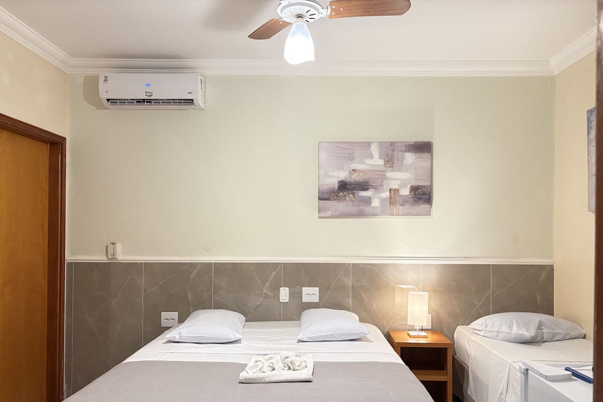 Une chambre d’hôtel comprenant un lit, des tables de chevet, un ventilateur de plafond, un appareil de climatisation et une œuvre d’art accrochée au mur.