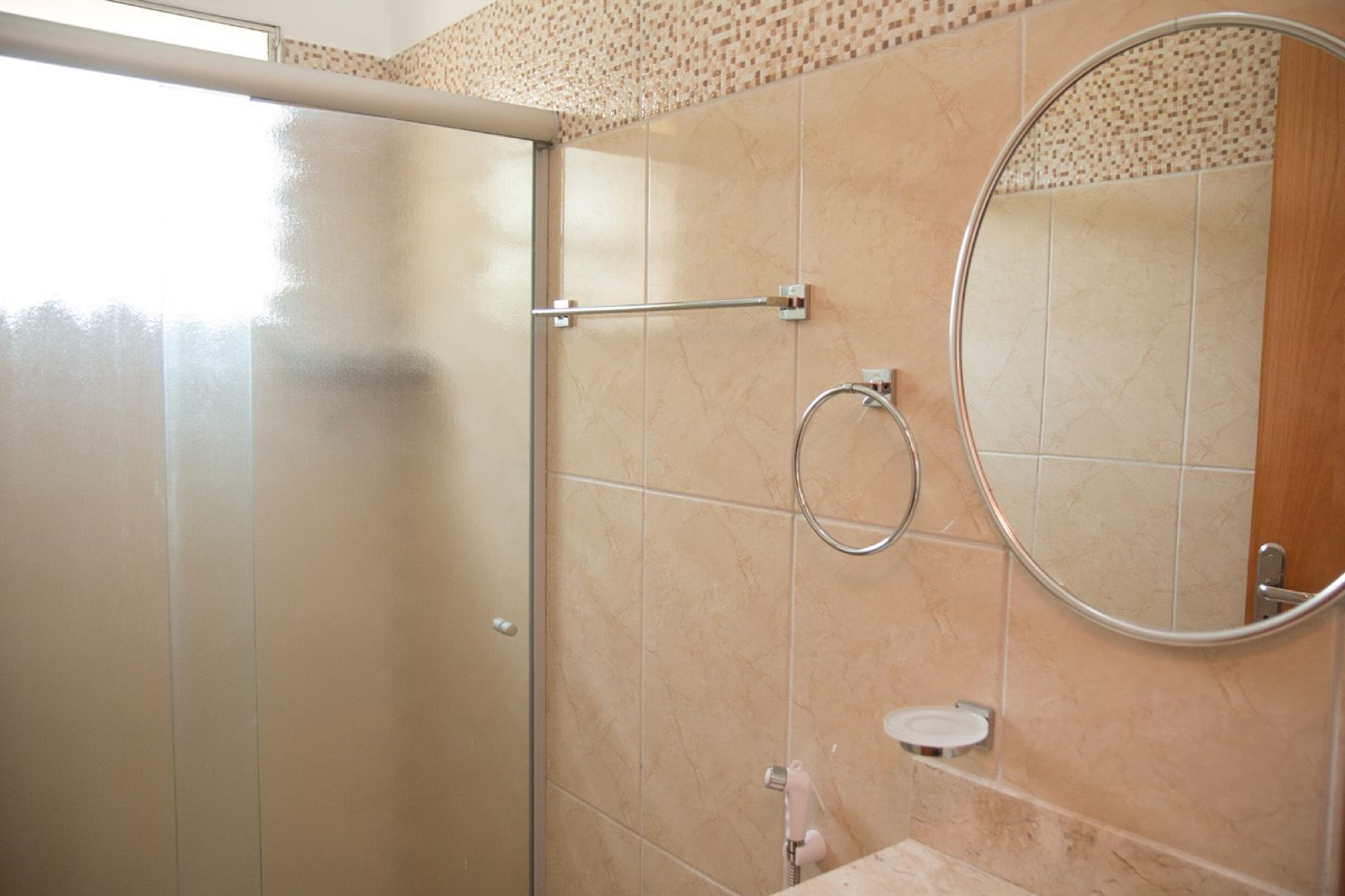 Un baño con mampara de vidrio, toallero, inodoro y espejo.