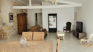 Amplia sala de estar con techo alto, una gran mesa de madera, muebles de mimbre, un televisor y una estantería.