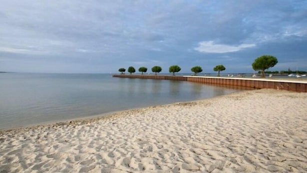 Una playa arenosa con un pasaje de madera y árboles.