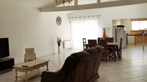 Un salón espacioso con sofá, una mesa de comedor con sillas, una zona de cocina y un televisor.
