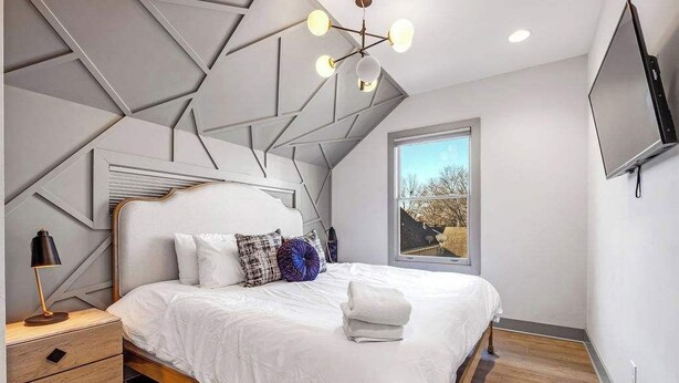 A modern bedroom with a geometric ceiling design, a large bed with white bedding, a nightstand, and a TV mounted on the wall. - Downtown Private Backyard Oasis 5 min to Broadway (Nashville)