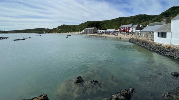 A coastal town with clear waters, boats, and a stone wall along the beach.
