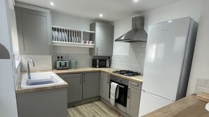 A modern kitchen with grey cabinets, a built-in oven, a microwave, and a stainless steel range hood.