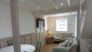 A living room with a white sofa, a small table, and a TV mounted on the wall.