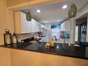 A kitchen with white cabinets, a black countertop, and a window with blinds.