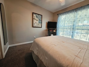 Ein Hotelzimmer mit einem großen Bett, einem Flachbildfernseher, einem gerahmten Bild an der Wand und einem Fenster mit Vorhängen mit Sternenmuster.