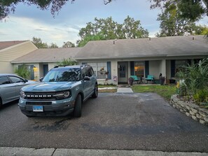 Ein Wohnhaus mit Auffahrt, einem parkenden Geländewagen und einer Veranda mit Sitzgelegenheit.