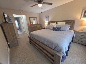 A bedroom with a bed, nightstands, a dresser, a ceiling fan, and a door leading to another room.