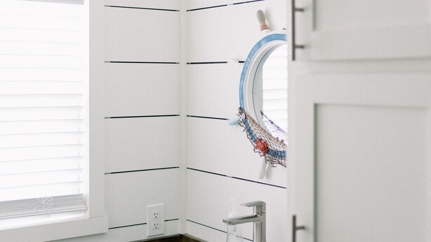Une salle de bain avec un lavabo blanc, un miroir et une fenêtre avec des stores.