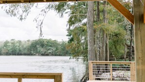 Une terrasse en bois surmontée d’un toit en métal, d’où l’on a vue sur un lac paisible entouré d’arbres.
