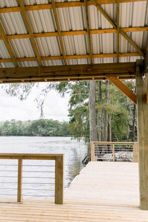 Une terrasse en bois surmontée d’un toit en métal, d’où l’on a vue sur un lac paisible entouré d’arbres.