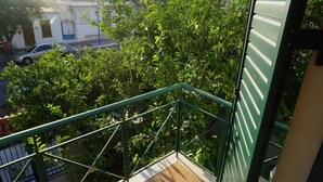 A balcony with a green metal railing overlooking a street with parked cars and buildings. - Garden House (Kalamata)