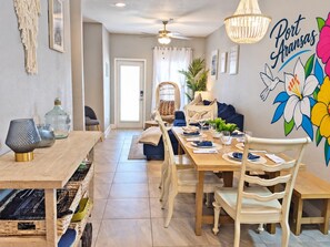 Comedor con mesa de madera dispuesta para cuatro, sillas, candelabro y un mural con pájaros y flores.