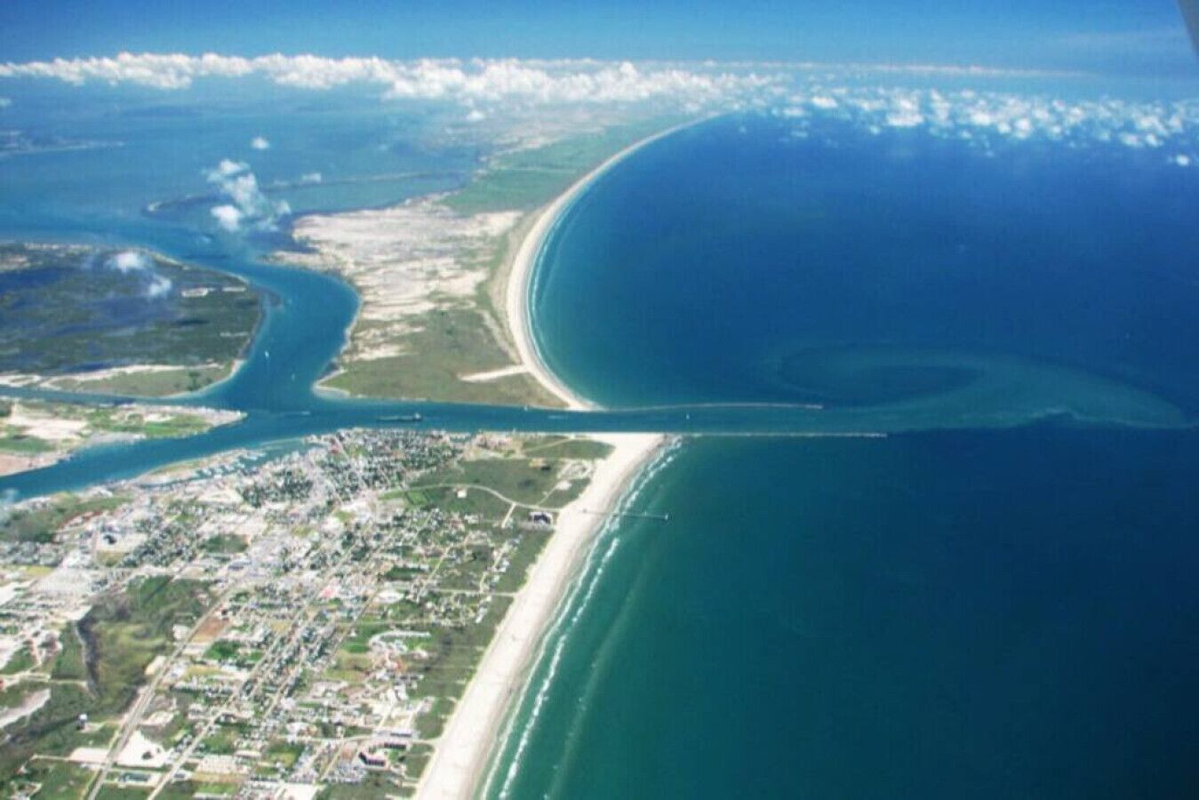 Vue aérienne d’une zone côtière comprenant une plage, une étendue d’eau importante et un paysage urbain.