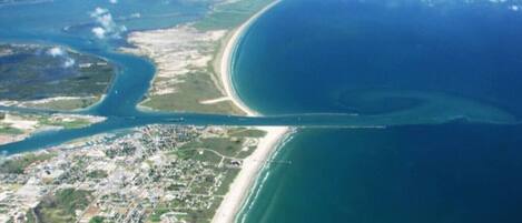 Vue aérienne d’une zone côtière comprenant une plage, une étendue d’eau importante et un paysage urbain.