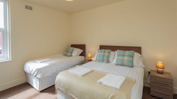 A bedroom with two beds, each with a nightstand, a lamp, and a window. - Cherry Property - Coconut Suite (Blackpool)