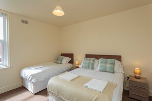 A bedroom with two beds, each with a nightstand, a lamp, and a window.